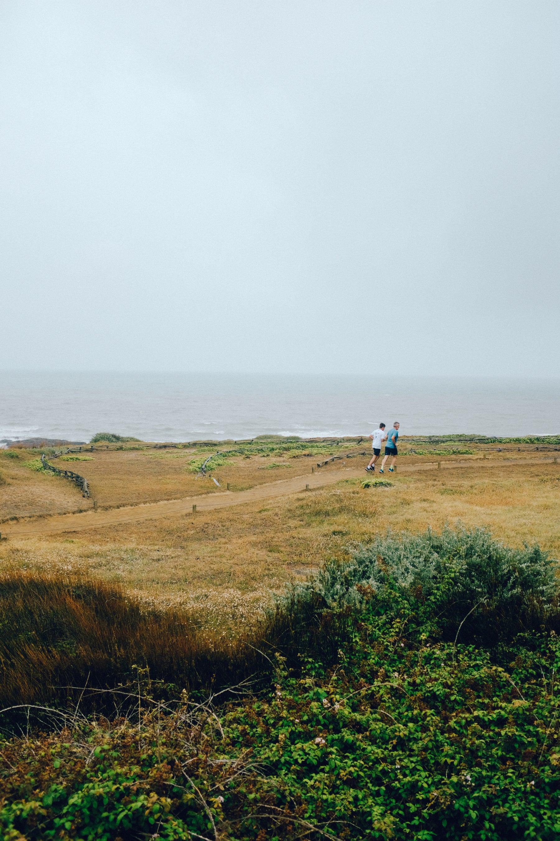 Two endurance runners rehearsing a hydration plan on an exposed coastal trail
