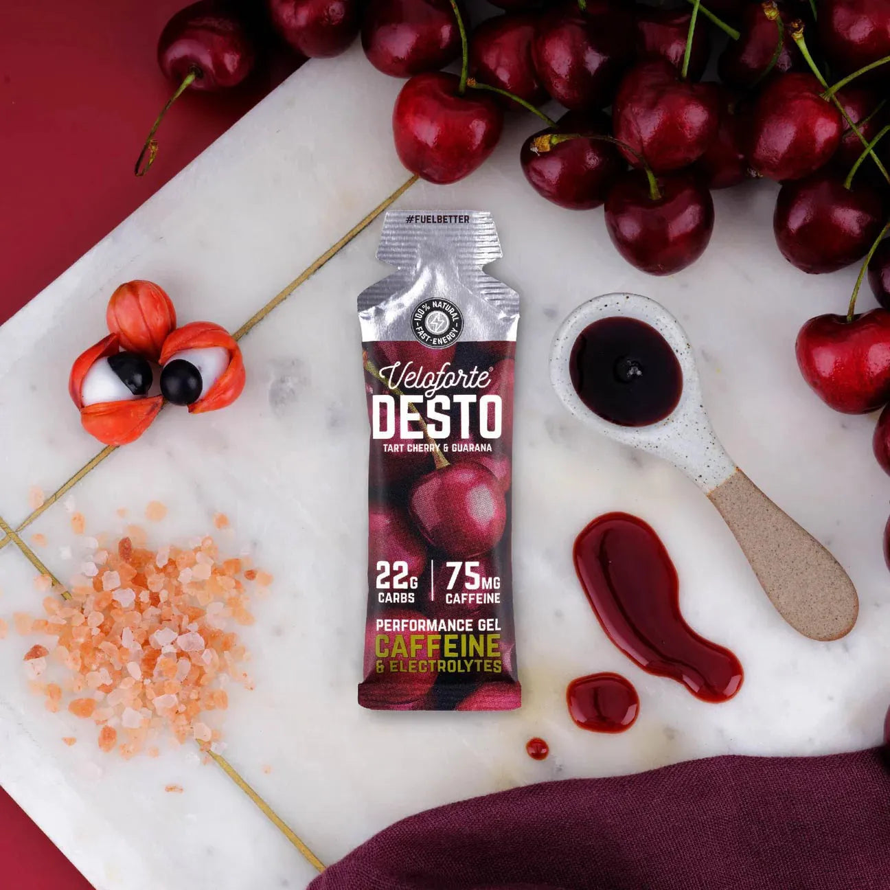 Veloforte Desto energy gel with caffeine on marble, surrounded by cherries, guarana, salt, and sauce.