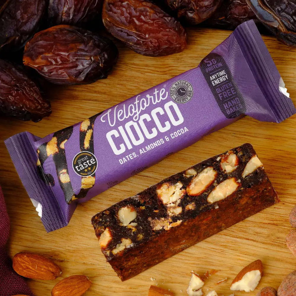 Veloforte Ciocco energy bar with dates, almonds, cocoa, packaging and ingredients on wood.