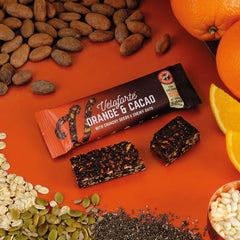 Veloforte Orange &amp; Cacao energy bar with oats, cacao beans, orange slices, and seeds on orange background